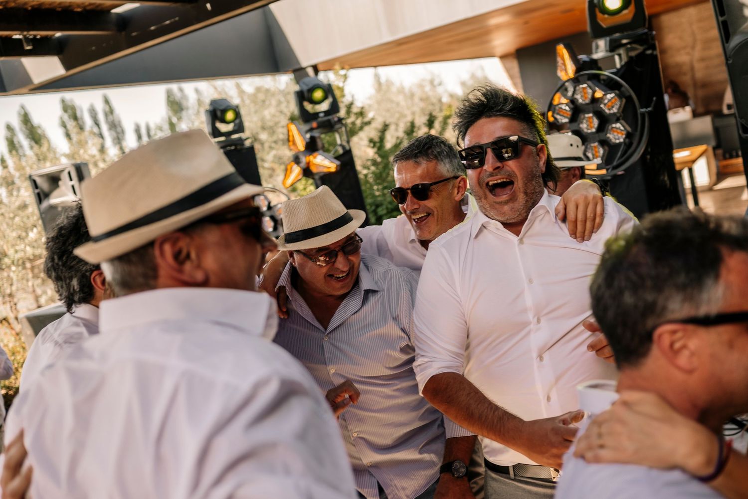 Wedding party guests dressed in white celebrate and dance together at an outdoor reception venue.