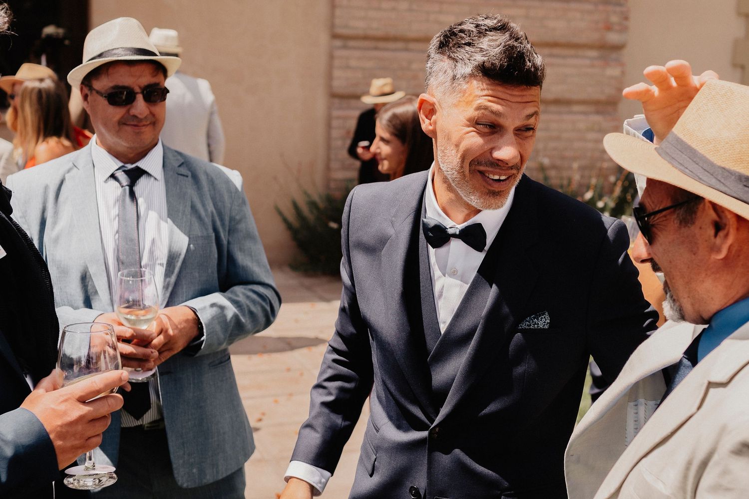 Groomsmen in gray suits and sunglasses share laughs during an outdoor wedding celebration.