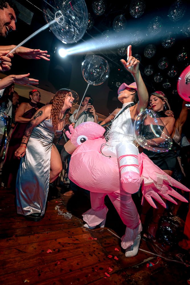 Energetic crowd at a nightclub party with a person in a pink inflatable costume dancing under blue lights. wedding in mendoza