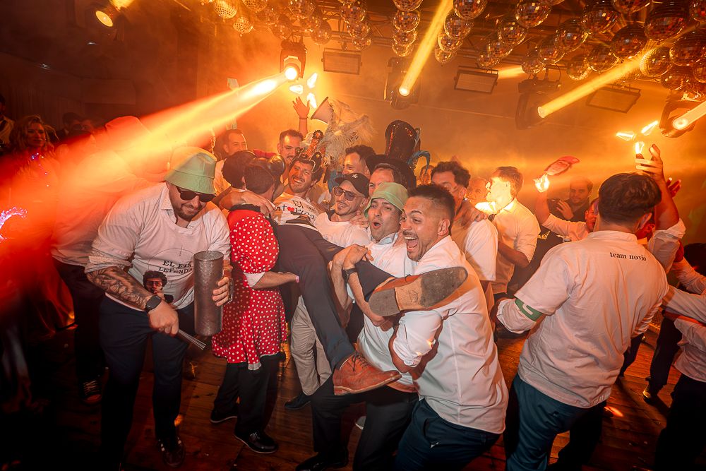 Energetic crowd dancing and celebrating at a lively nightclub party under red and orange lighting effects.