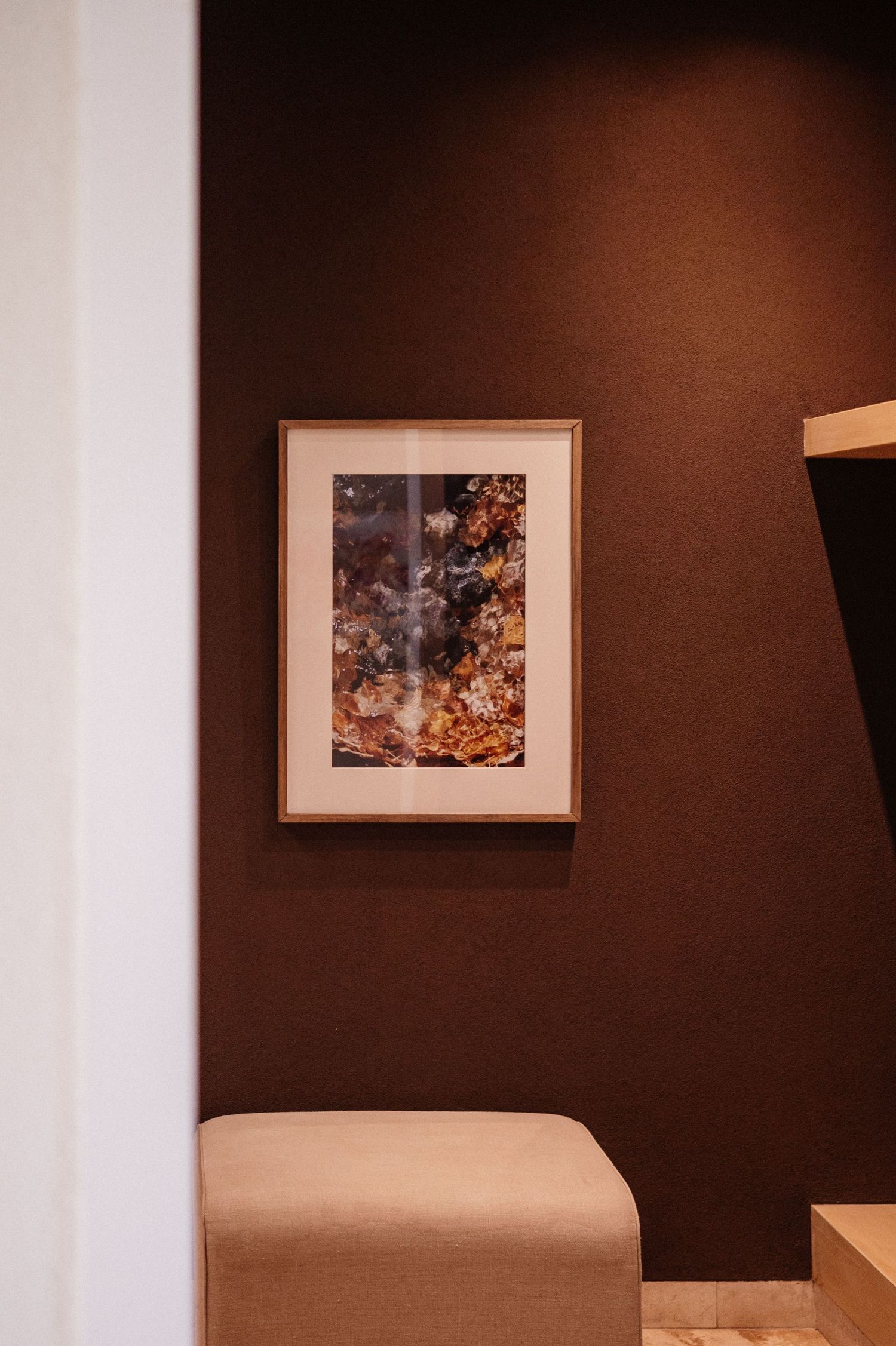 Framed floral artwork on a dark brown wall above a beige upholstered bench in a modern interior.