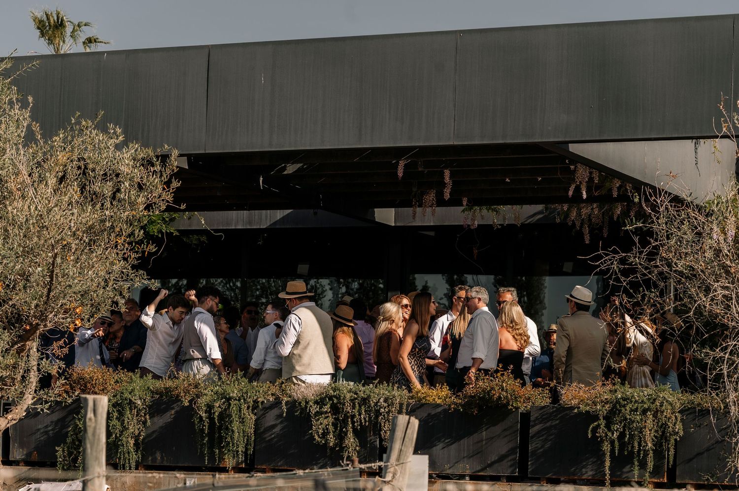 A group of people gathered outdoors at a modern building with glass windows during sunset.