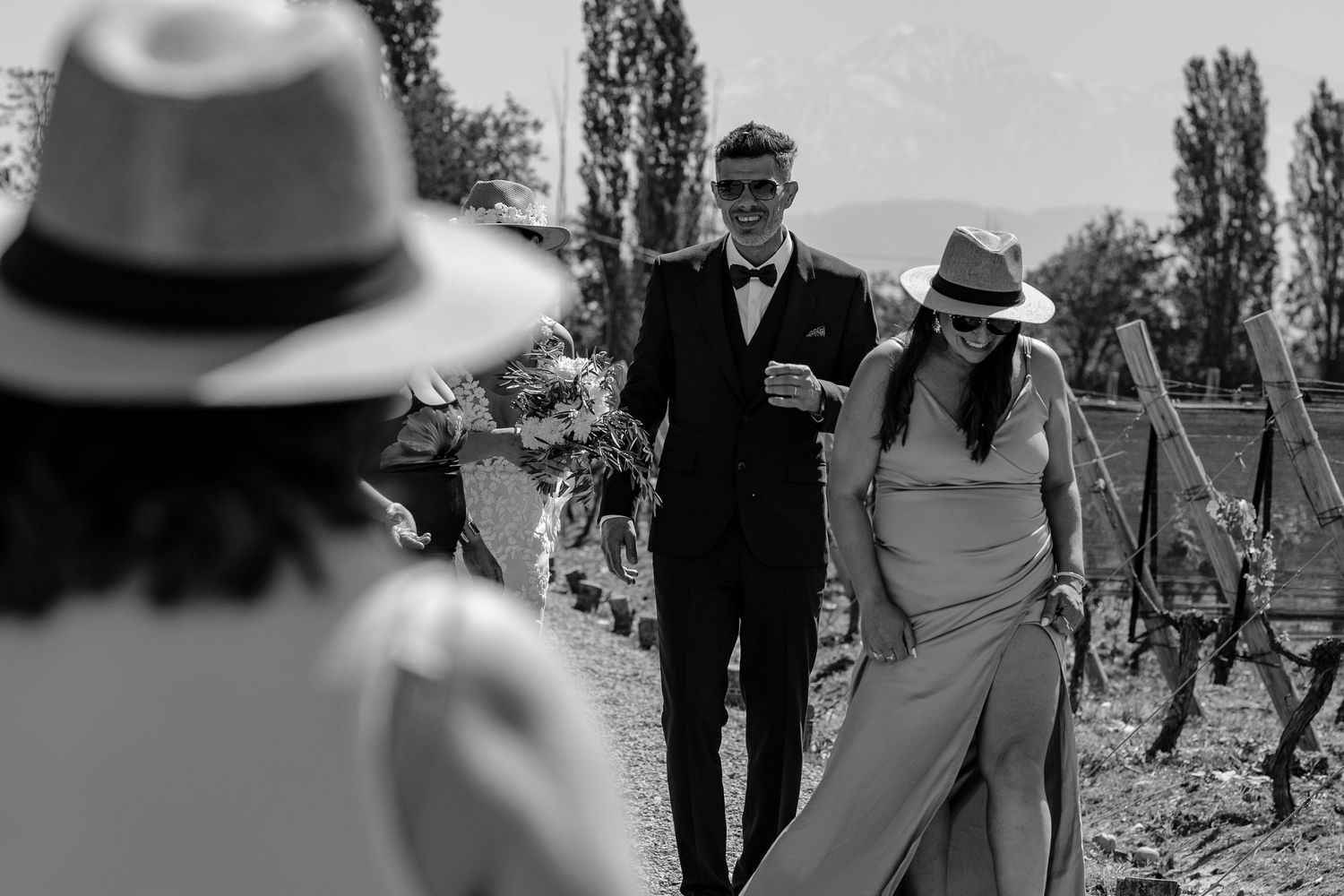 A romantic couple walks together outdoors during a wedding celebration with trees in the background.