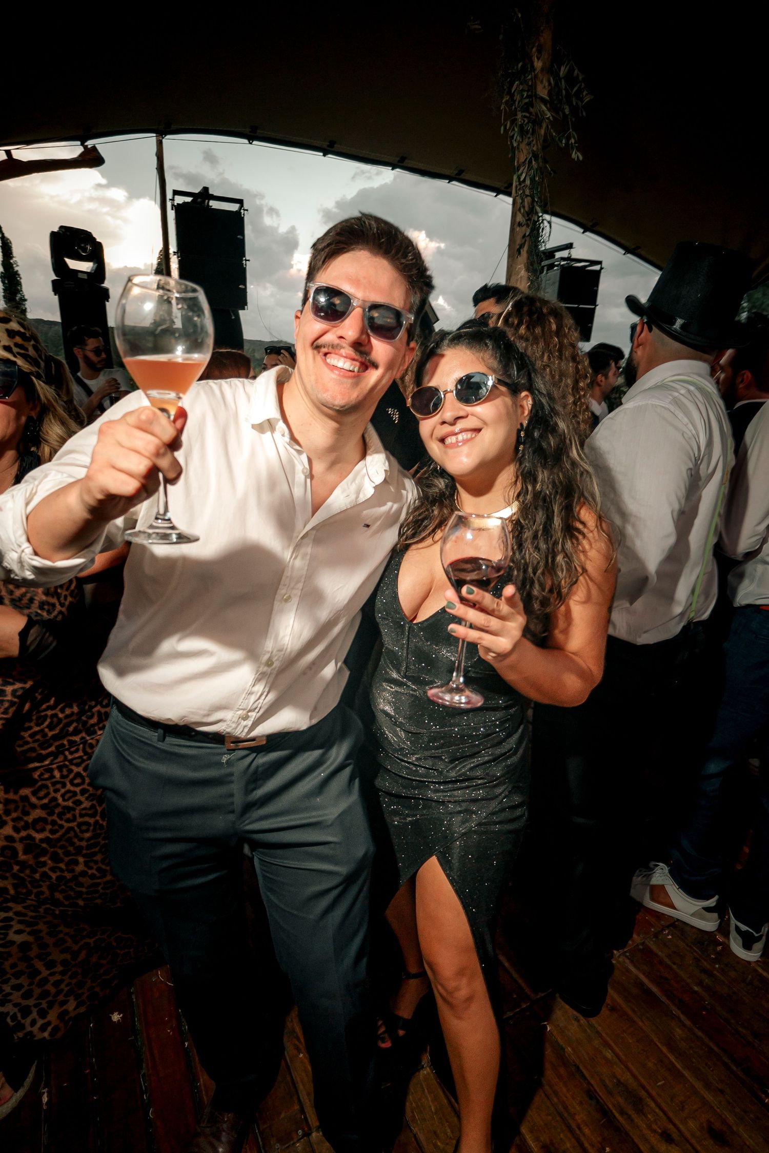 Party guests raise their drinks in celebration while dancing at a dimly lit indoor event.