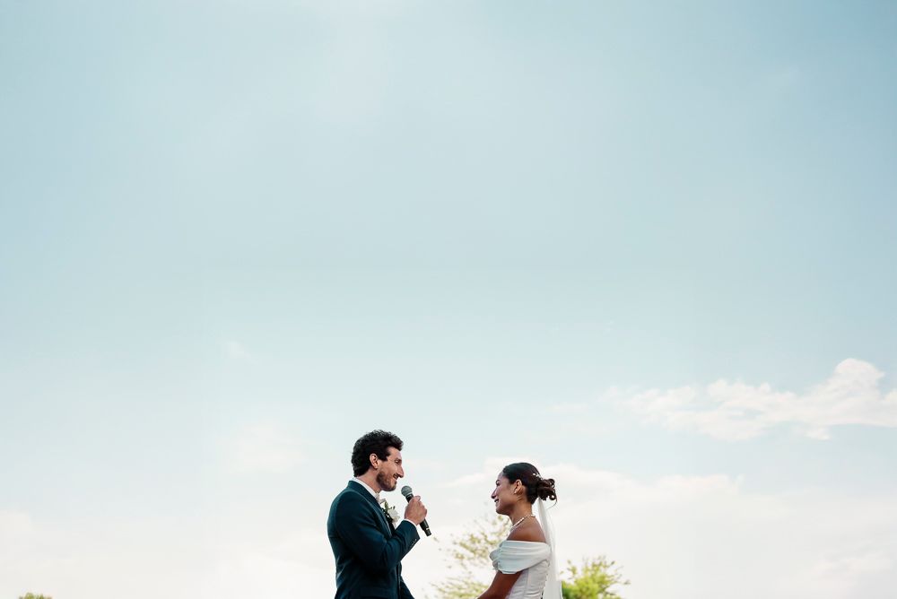 A couple shares an intimate moment against a bright blue sky during their outdoor wedding ceremony.