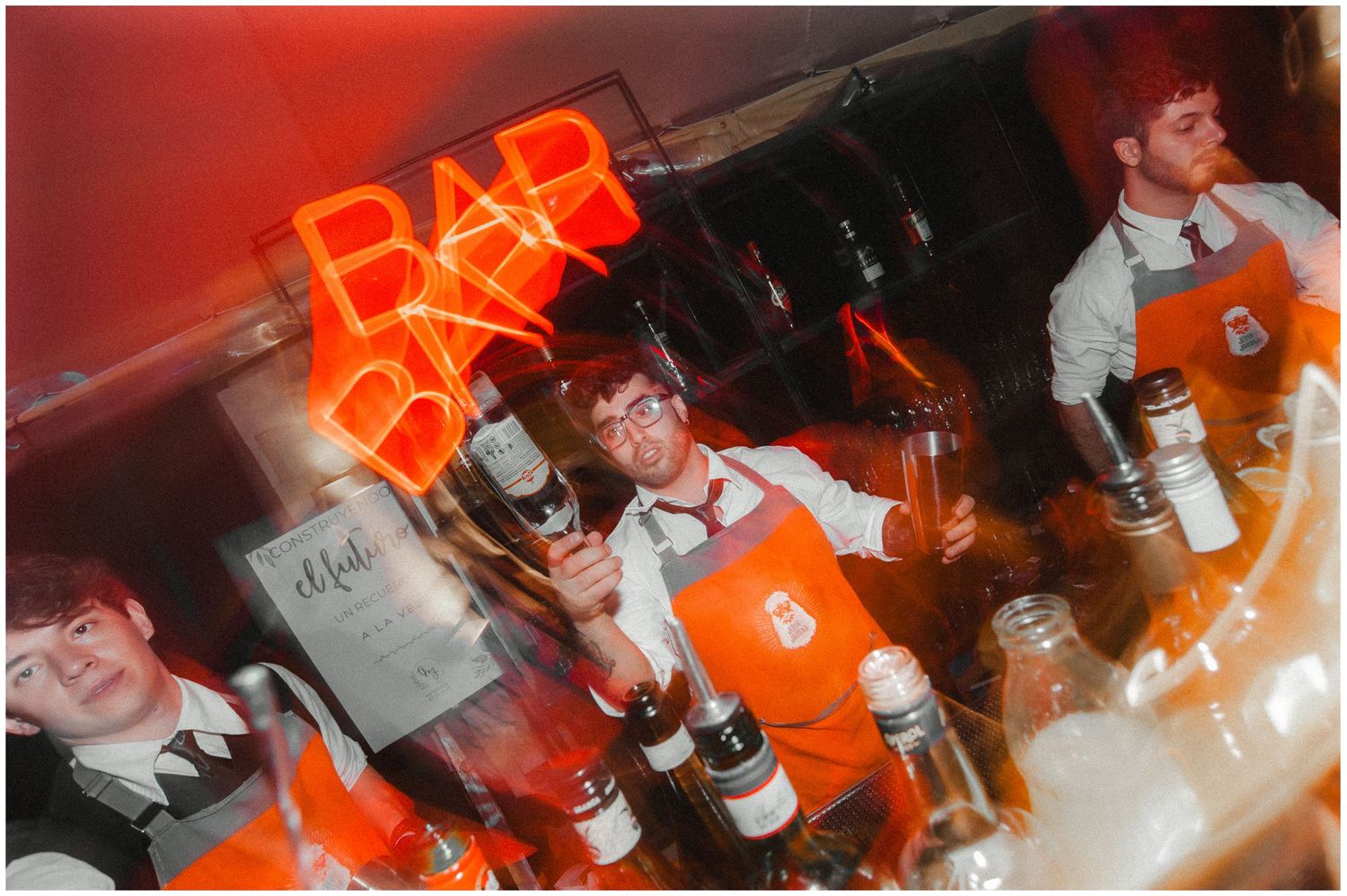 People enjoying drinks and socializing at a dimly lit bar with red neon lighting and bottles on display. fotografos de boda en mendoza