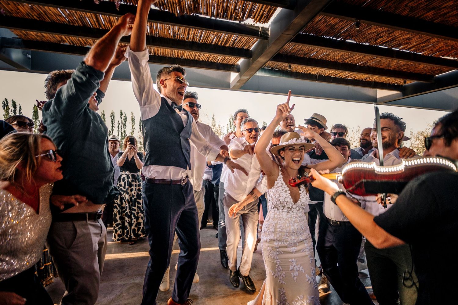 Wedding guests dancing and celebrating together on a rustic dance floor under wooden beams.