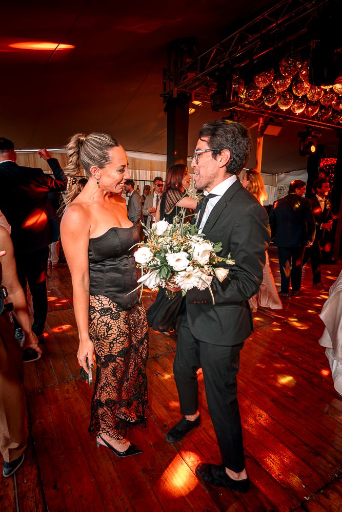 Couples dancing together at an evening reception with warm red lighting on a wooden dance floor.