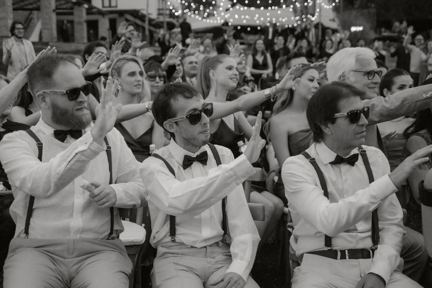 Black and white photo of a large crowd dancing in unison at an outdoor event in vintage attire. fotografos de boda en mendoza