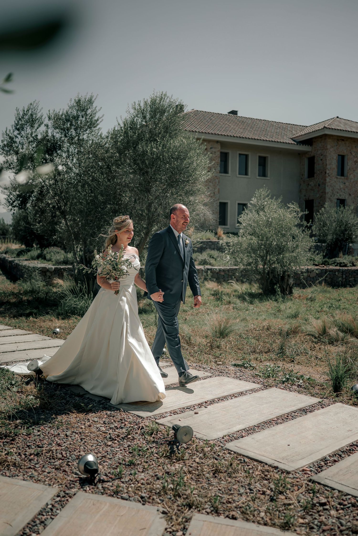 A couple in wedding attire walks along a concrete path surrounded by desert landscaping on their special day.