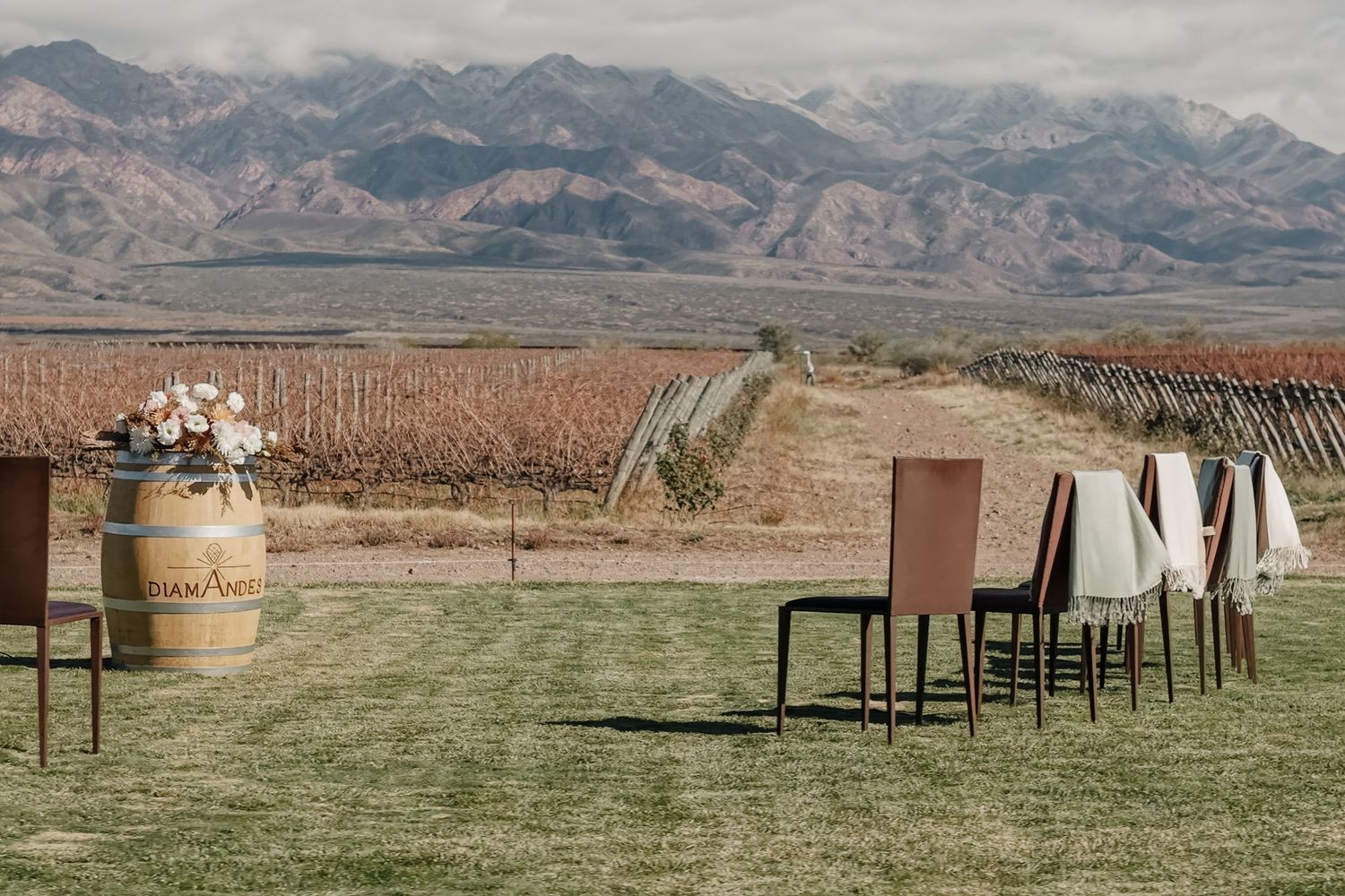 Outdoor winery wedding setup with wooden barrel, chairs, and stunning mountain vineyard backdrop.