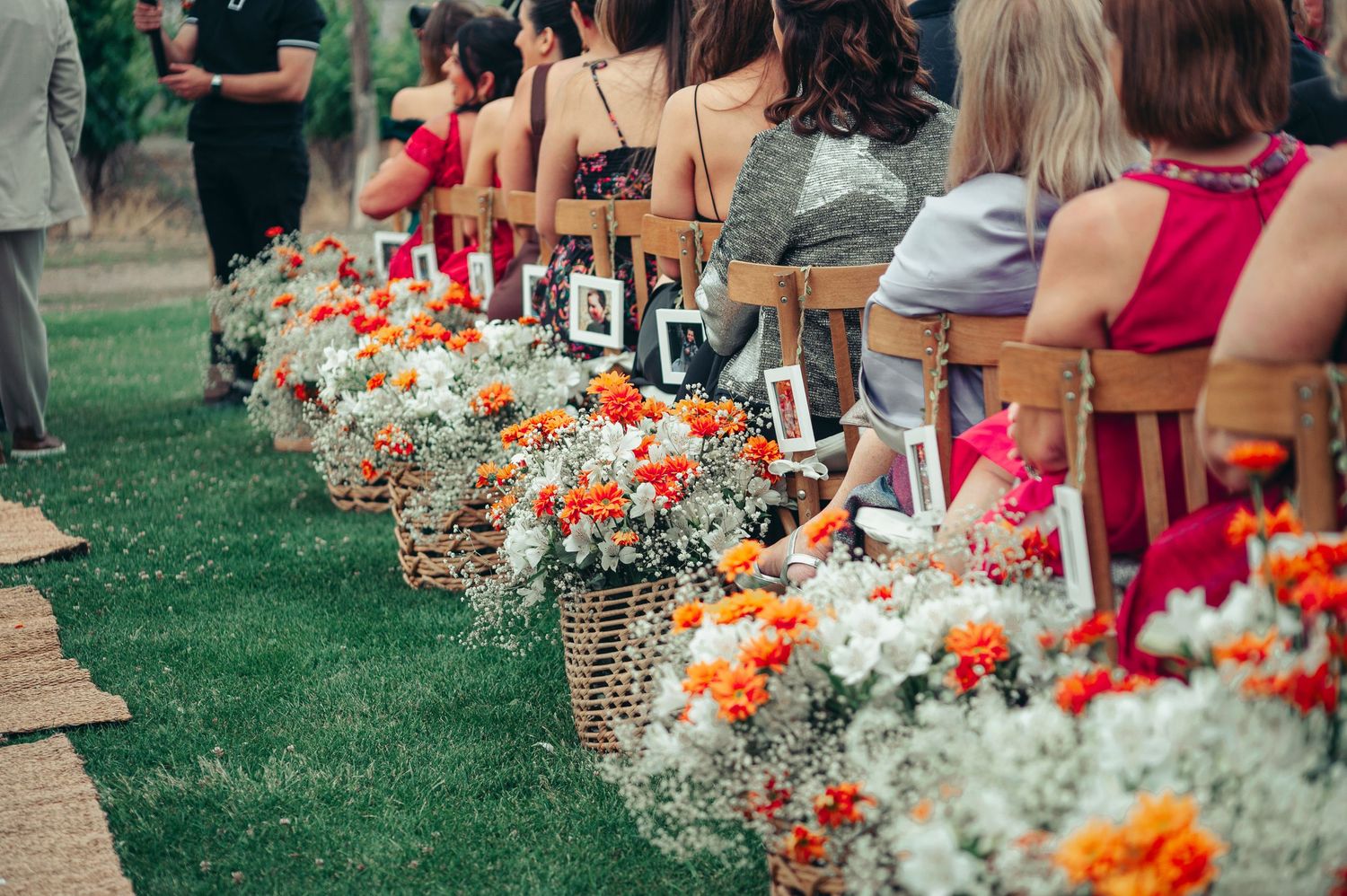 Wedding guests stand along a stone path lined with vibrant orange and white floral arrangements and photos. fotografos de boda en mendoza