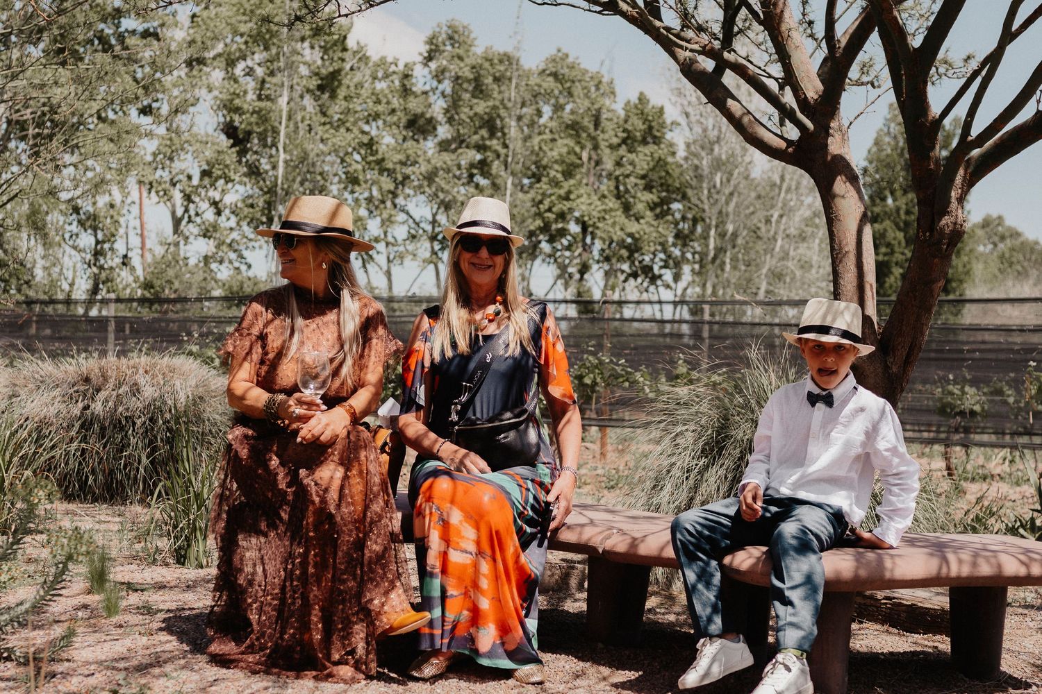 A group sits outdoors in a rural setting with trees and fencing visible in the background.