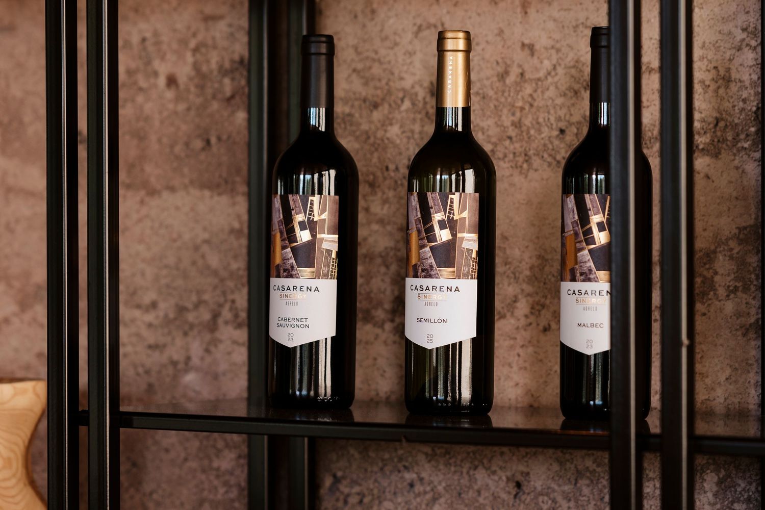 Wine bottles displayed on wooden shelves against a rustic stone wall in a cellar or tasting room.