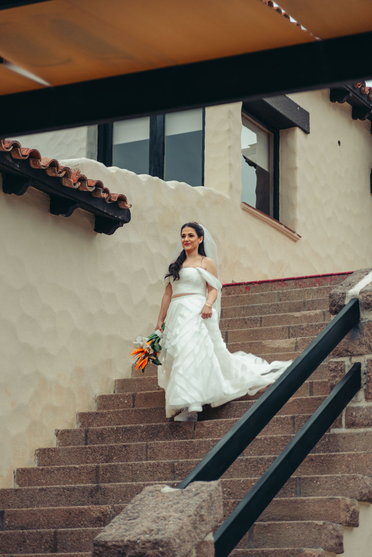 A person in a white wedding dress gracefully ascends stone steps at a Spanish-style venue.