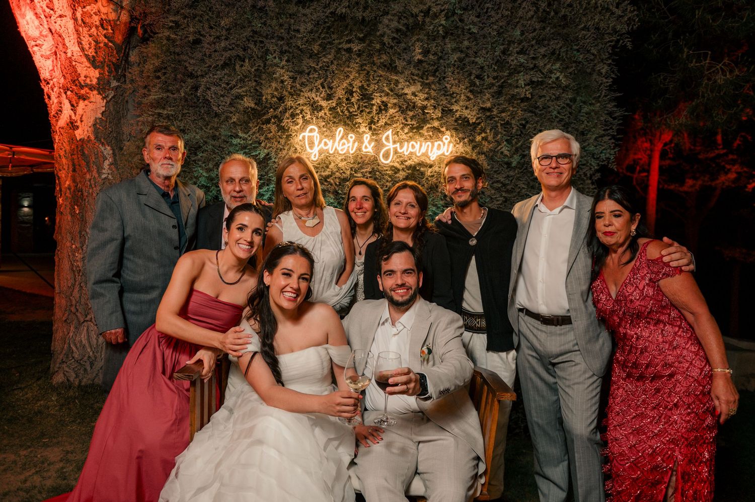 Wedding guests pose together in a series of candid group photos with red lighting at an evening reception.