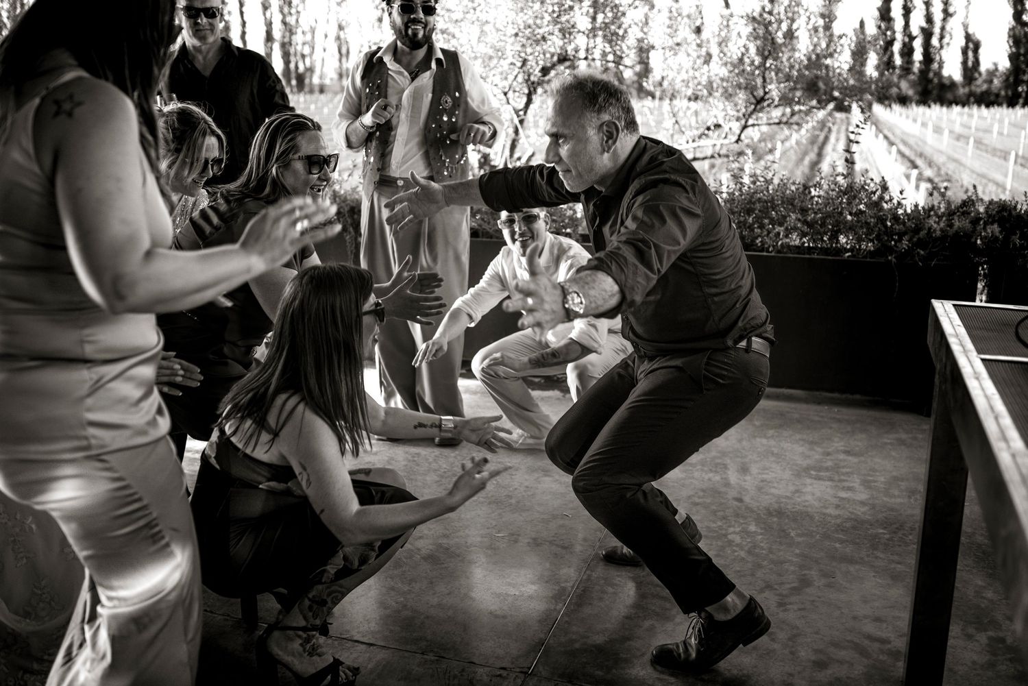Black and white photo of people dancing energetically at an outdoor party on a wooden deck.