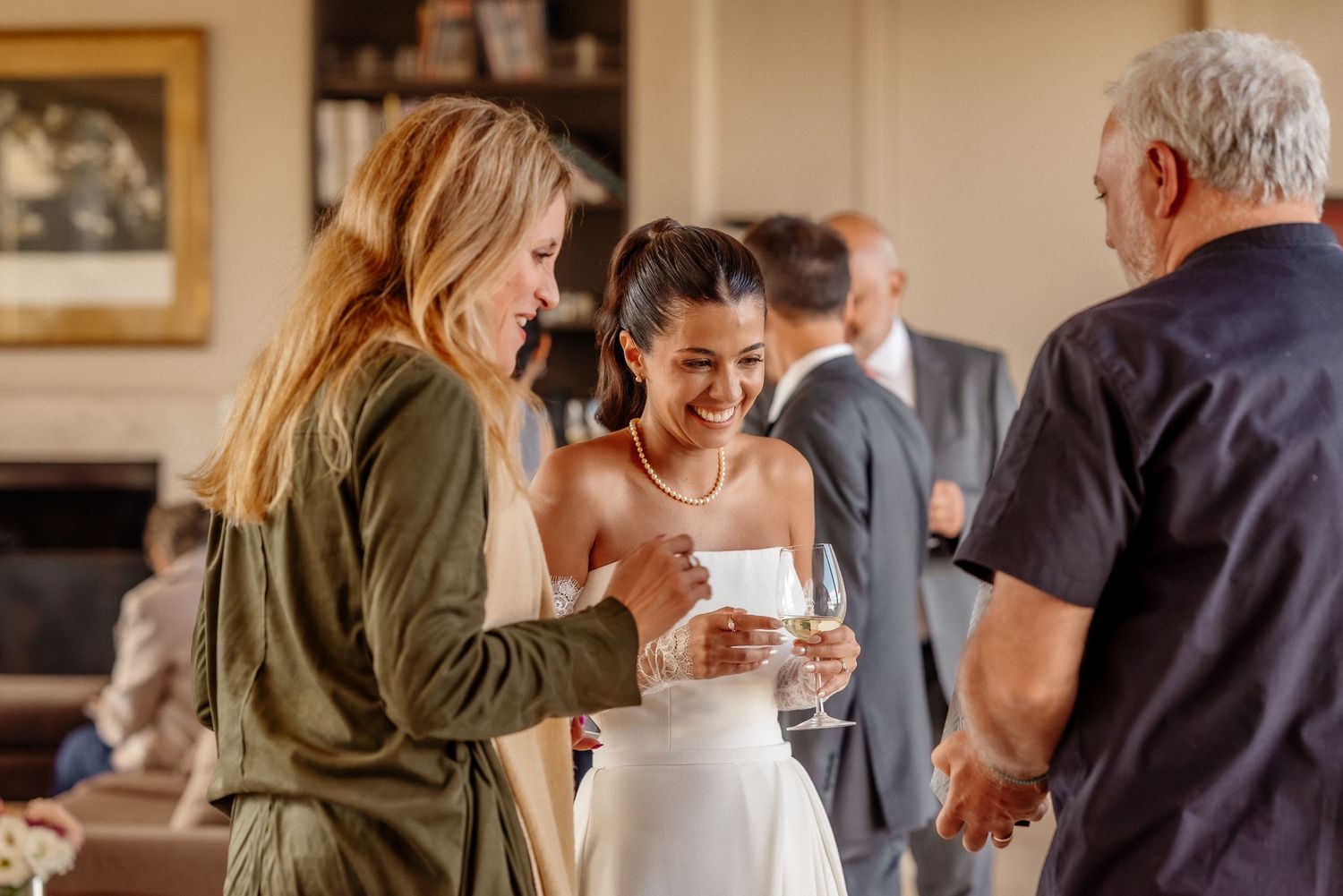 Bride in white dress laughing with guests at wedding reception, holding champagne glass in elegant indoor setting.fotógrafos de boda Mendoza