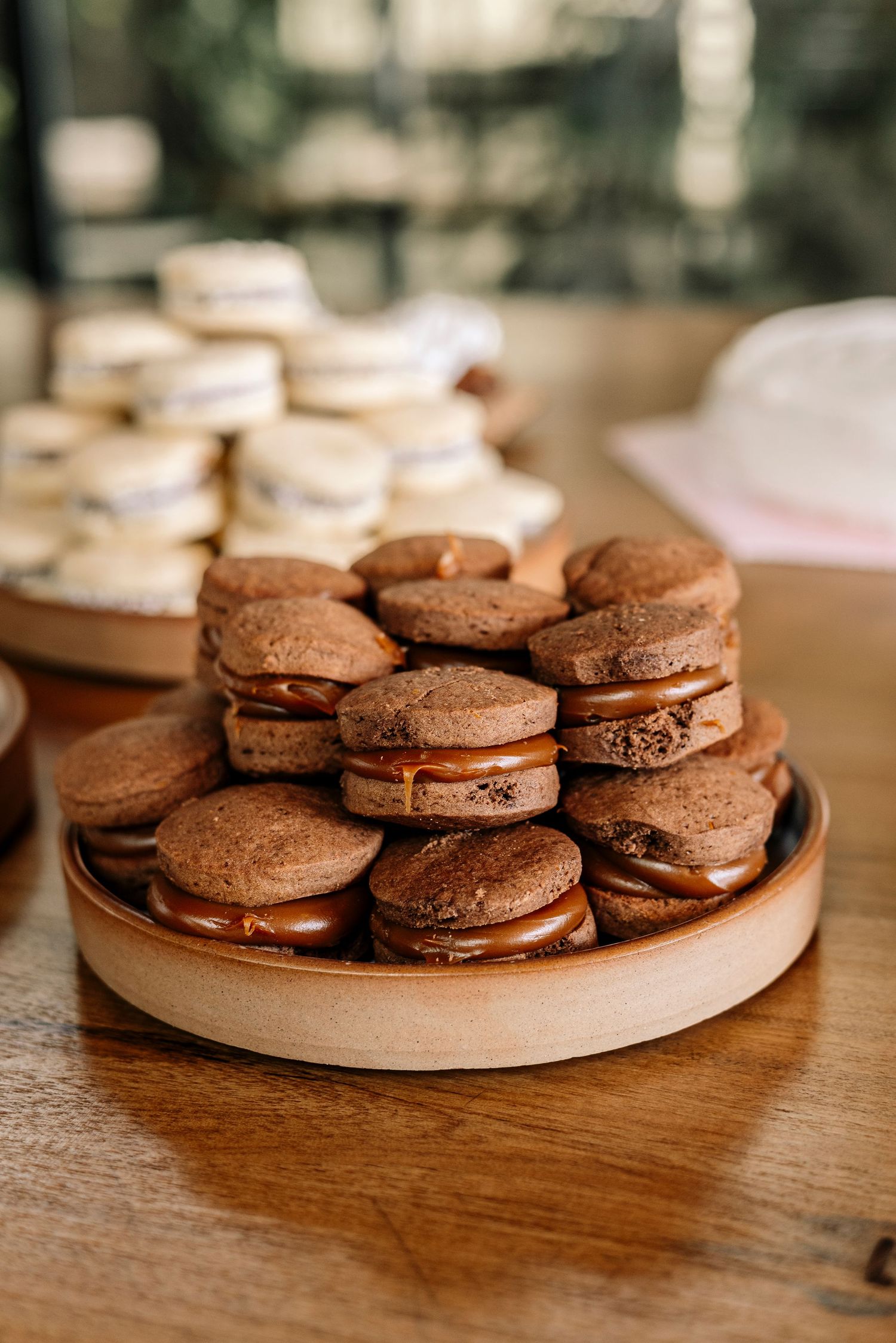 Chocolate sandwich cookies with creamy filling arranged on a round wooden plate in natural lighting.