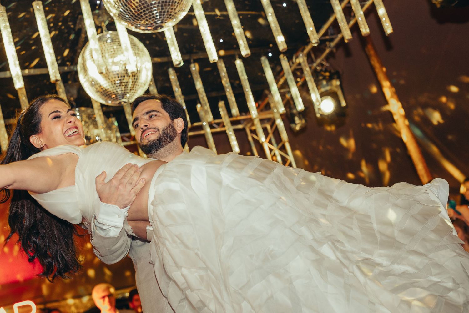 A couple shares a romantic dance at their wedding reception under glowing string lights and chandeliers.