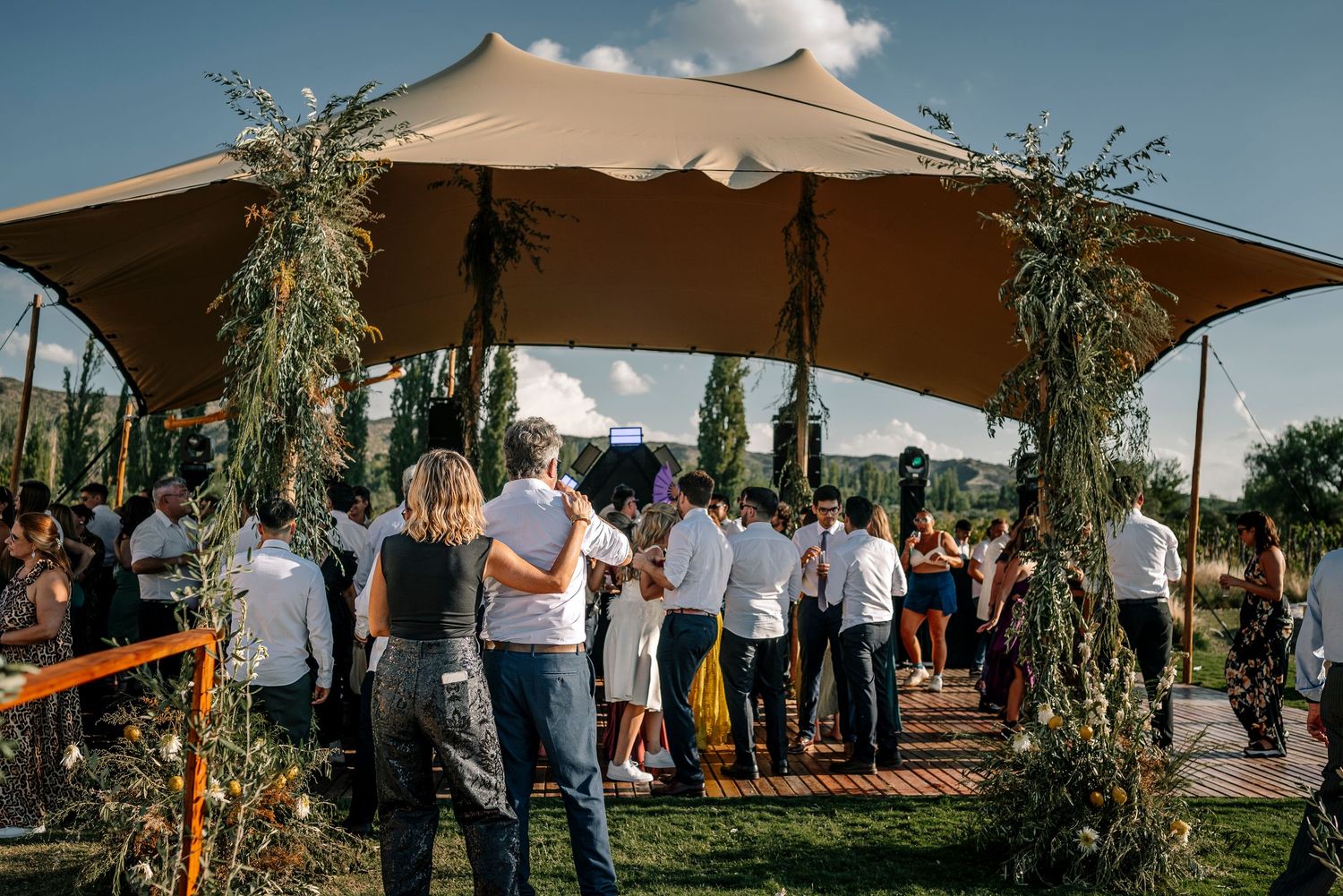 Outdoor wedding reception setup with beige umbrellas and natural greenery decorations under a blue summer sky. fotografos de boda en mendoza