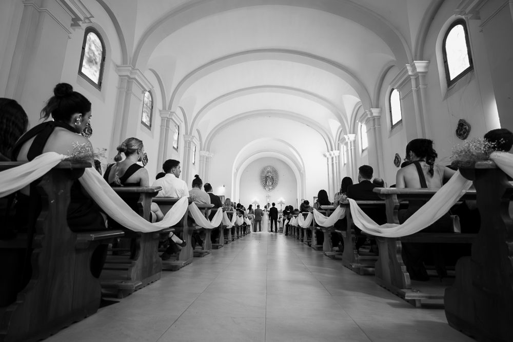 People sit in rows along the walls of a long, bright corridor with arched ceilings and windows. wedding in mendoza
