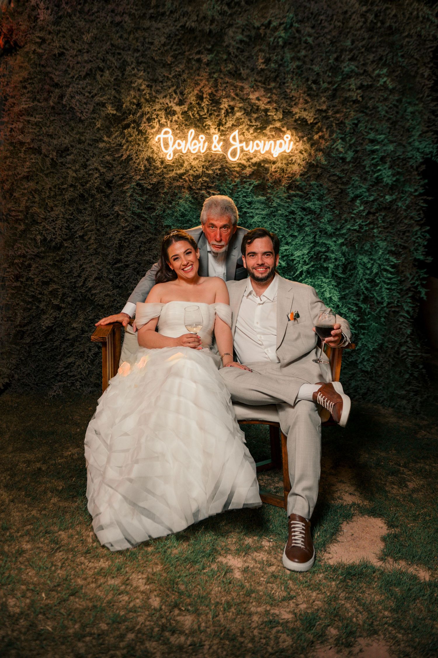 A couple sits together on grass at night with illuminated neon signage creating a romantic wedding atmosphere.