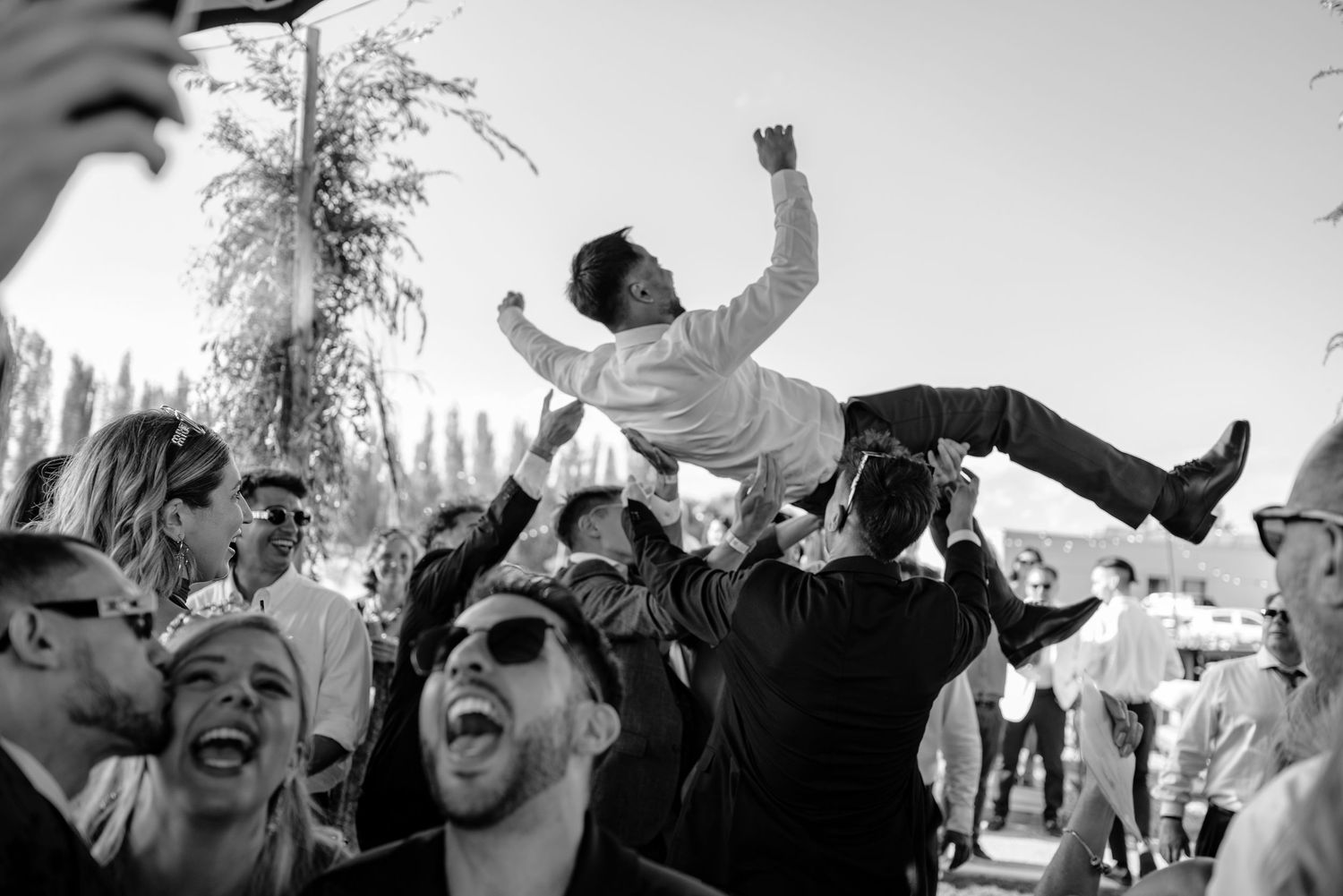 Black and white photo of a crowd celebrating and raising their arms at an outdoor event. fotografos de boda en mendoza