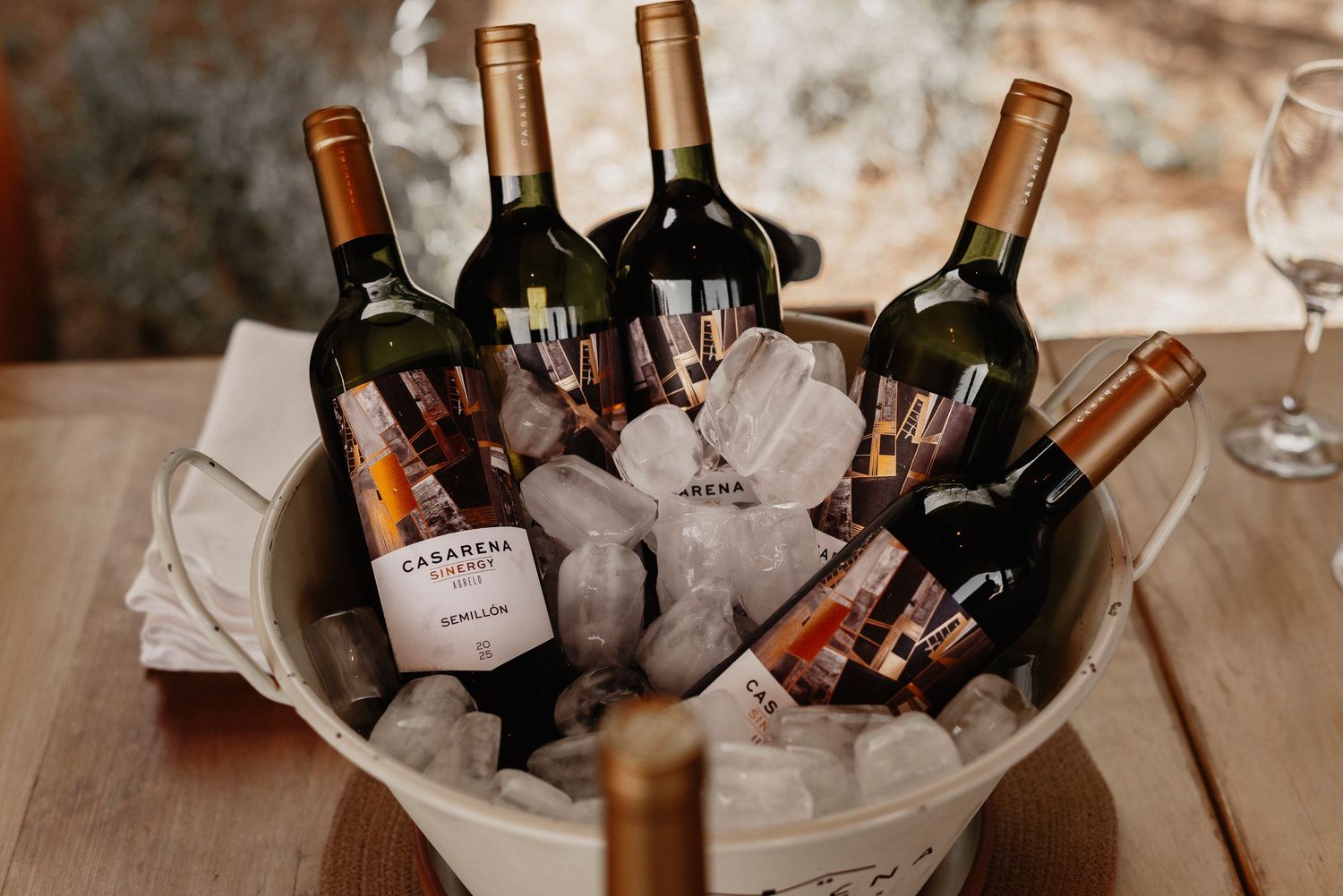 Wine bottles and glasses arranged on a rustic wooden surface with ambient lighting create an elegant party atmosphere.