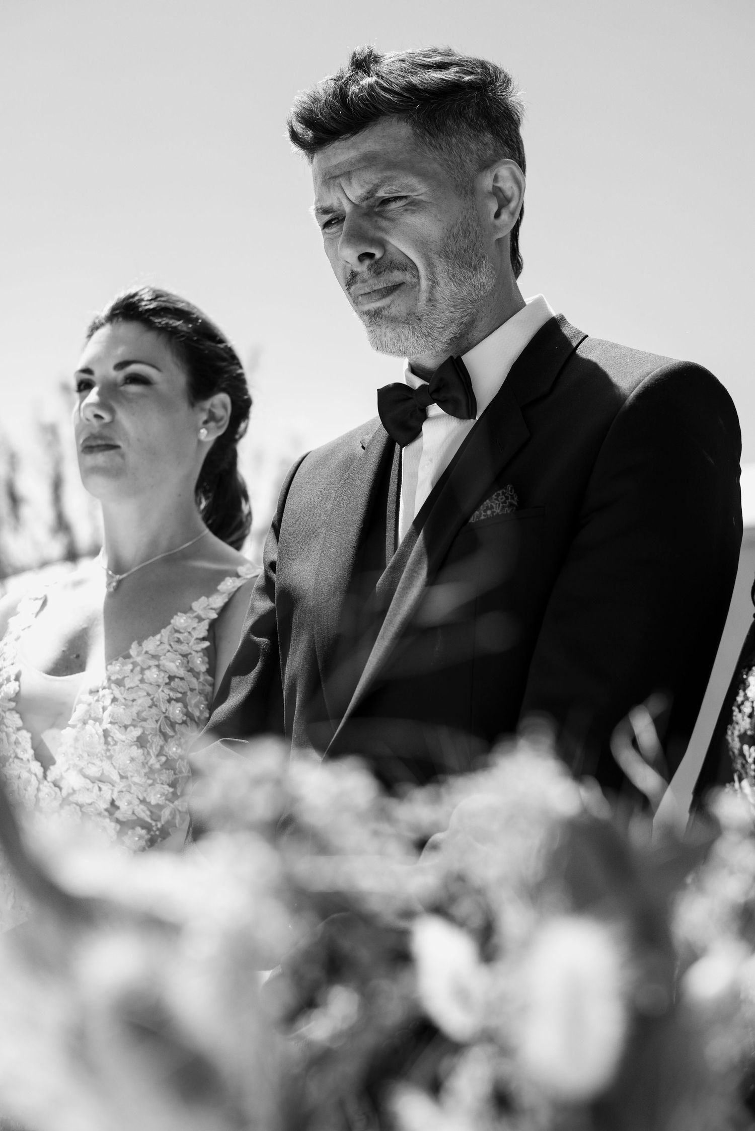 Black and white wedding photo sequence showing couple in formal attire gazing at each other through blurred foreground flowers.