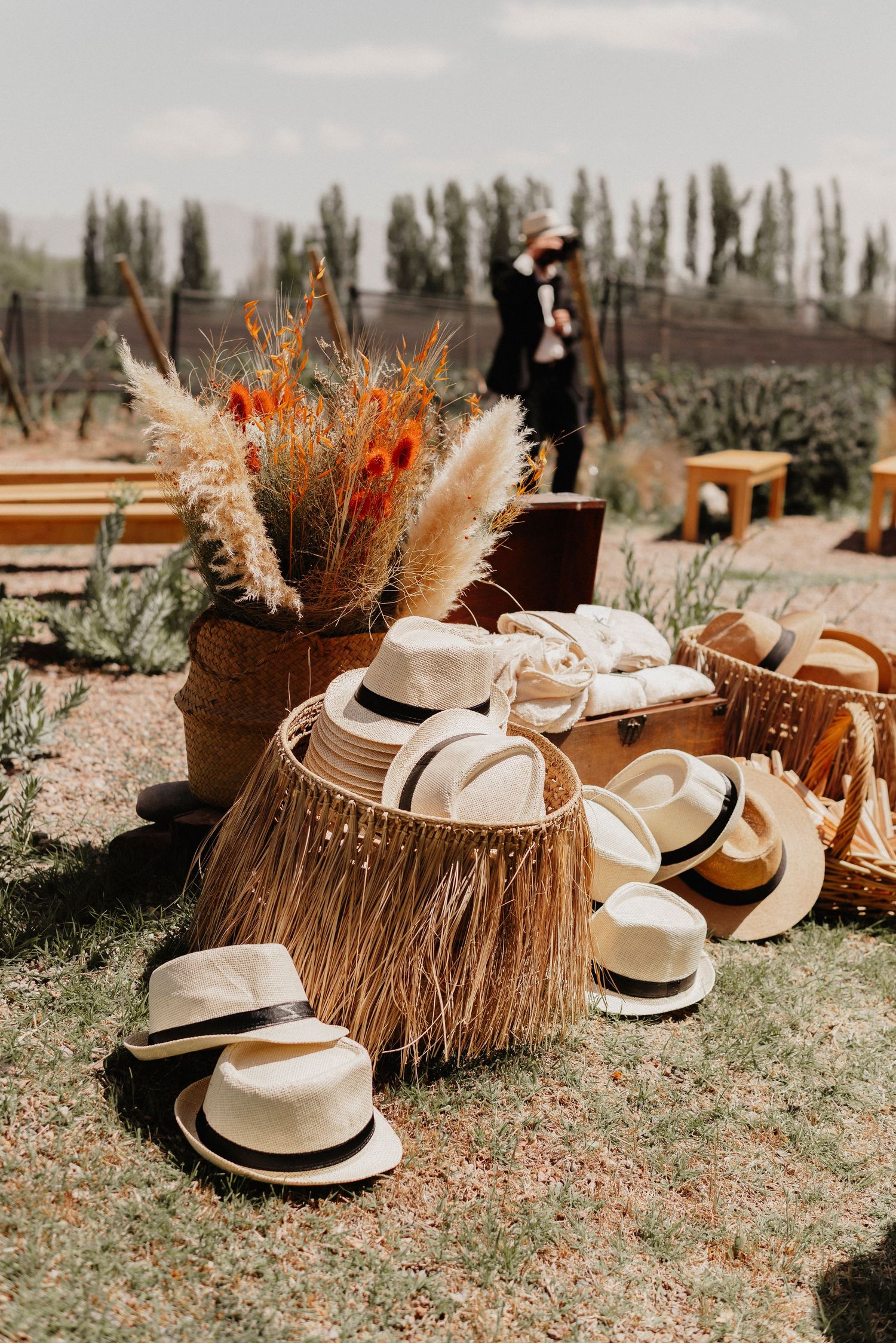 White Panama hats and dried floral arrangements create a rustic bohemian wedding decor display on grass.