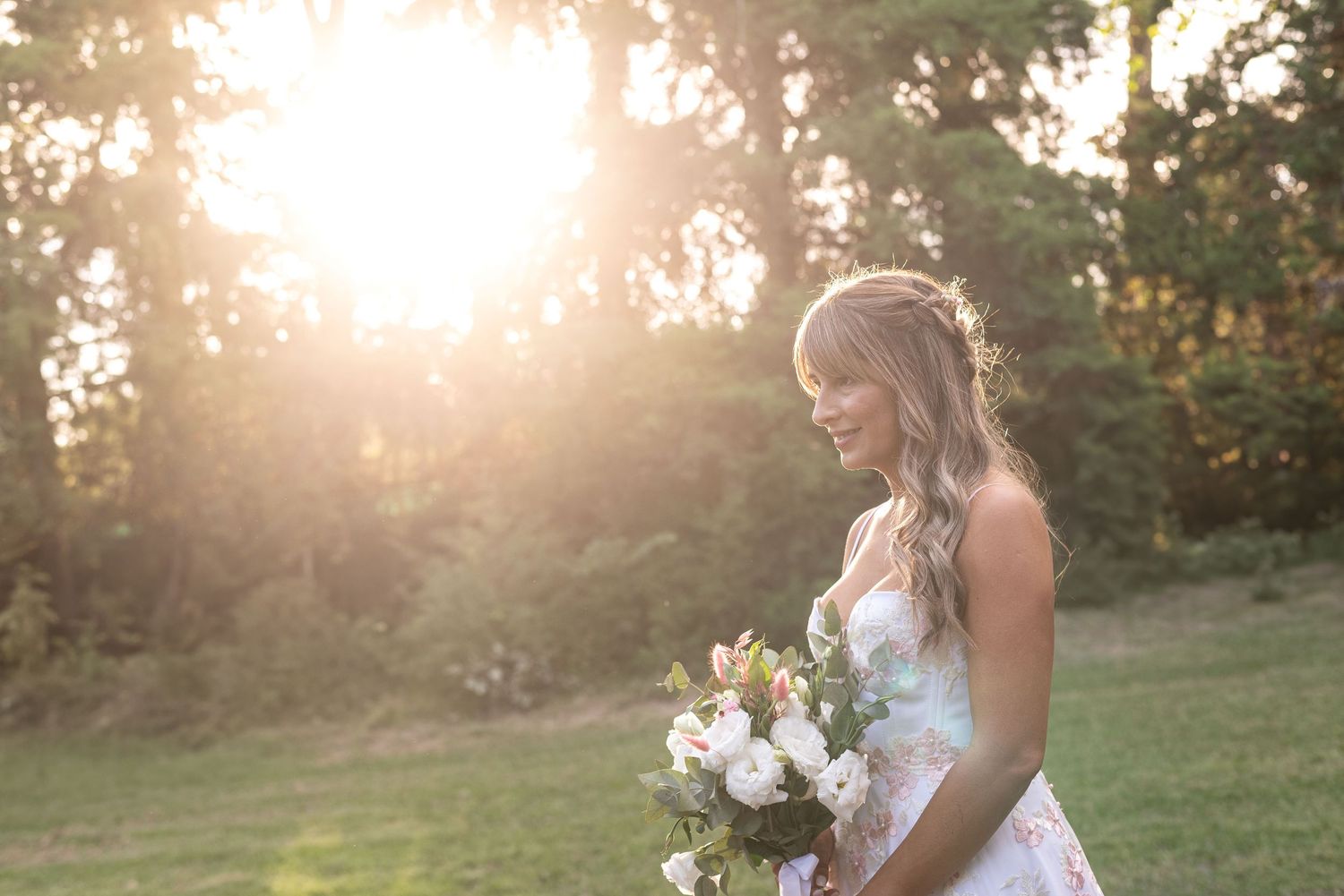 Bride holding bouquet in sunlit outdoor setting during golden hour.
