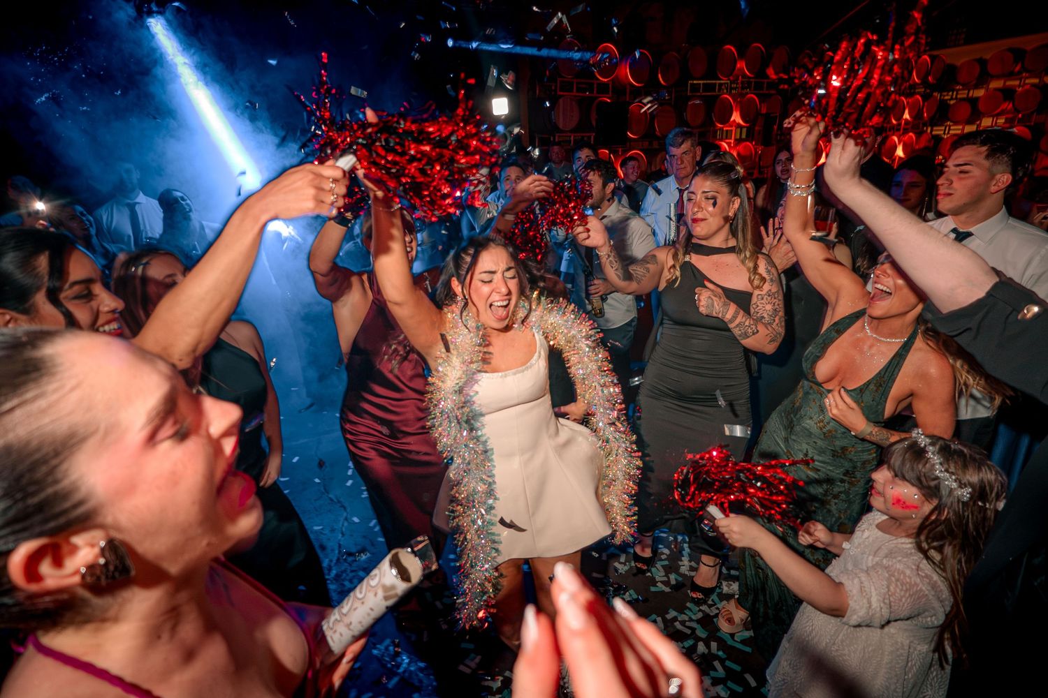 Bride celebrates with sparklers and confetti surrounded by guests at a lively wedding reception party.