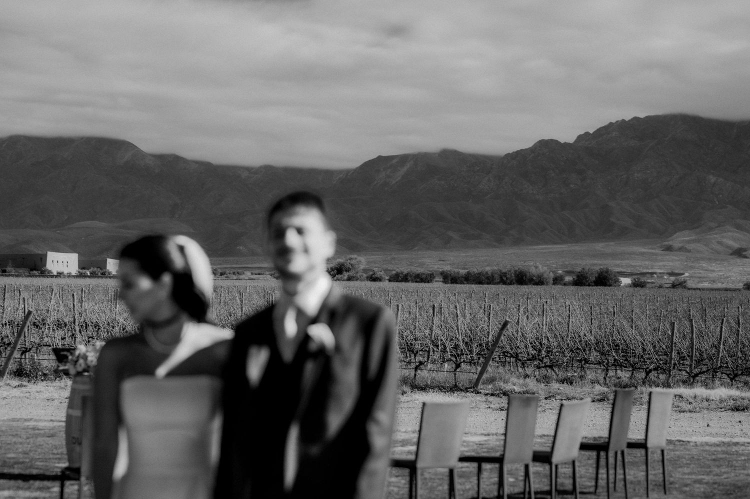 Black and white photo of a couple at a vineyard wedding with mountains in the background.