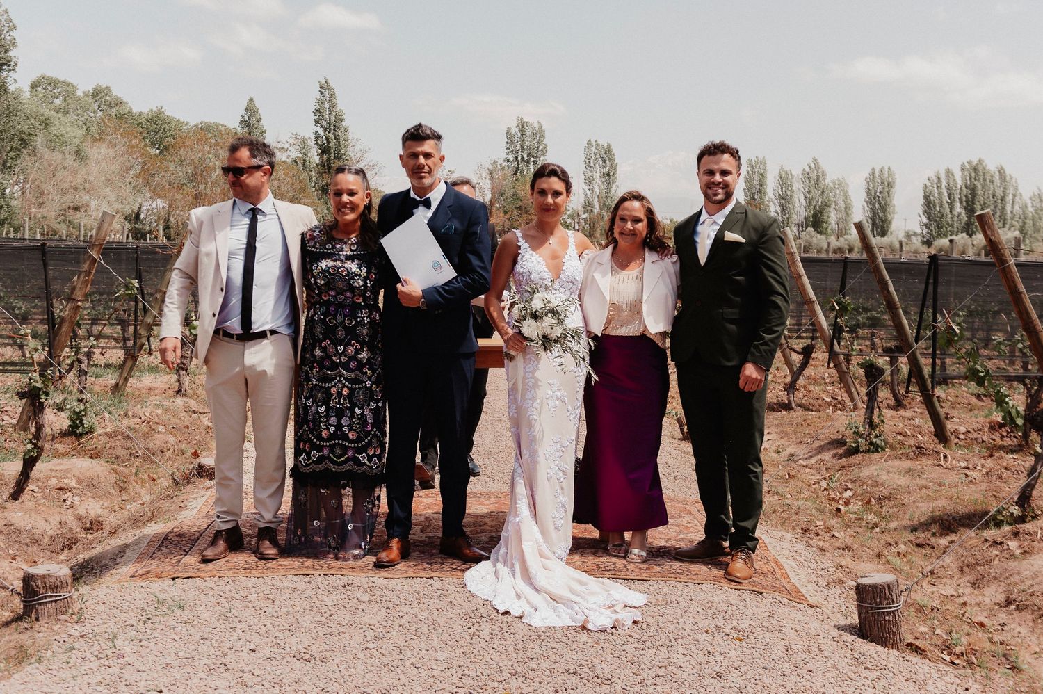 A wedding party poses in a desert landscape with cacti and mountains in the background during golden hour.