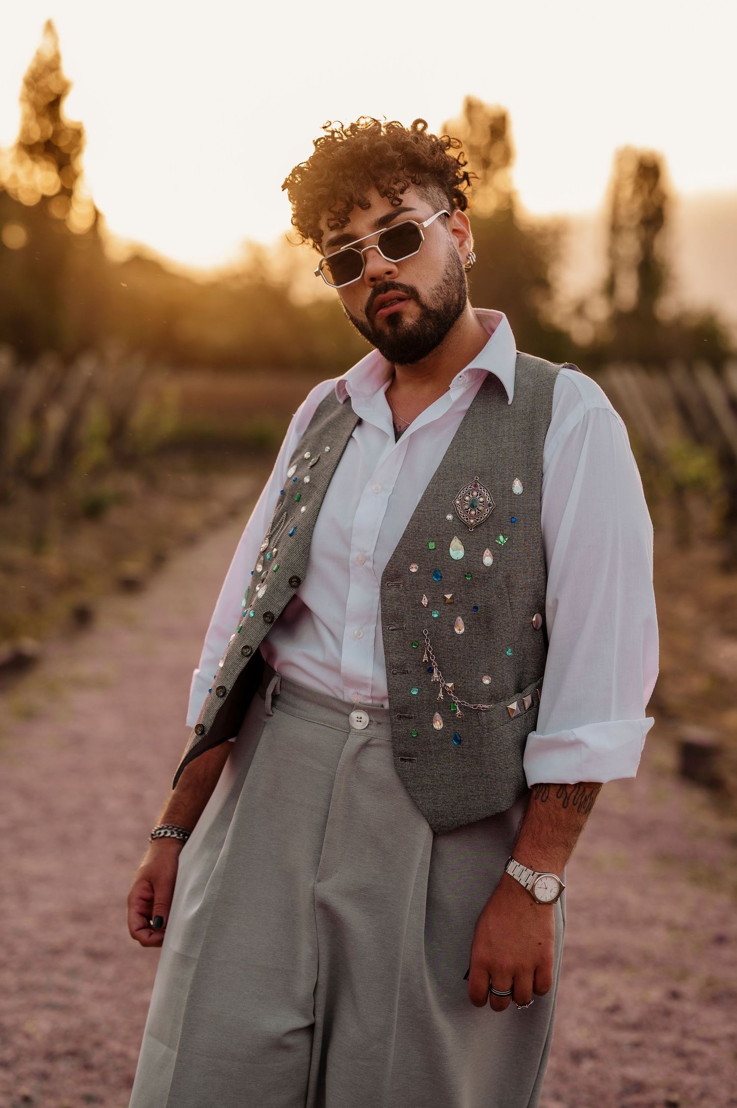A person wearing a gray vest and white shirt poses against a desert landscape at sunset.
