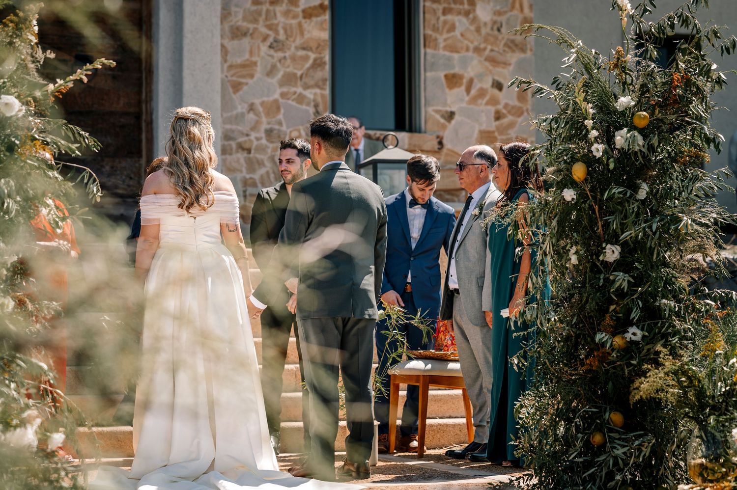 Romantic outdoor wedding ceremony setup with stone walls, wooden furniture and natural greenery decorations.