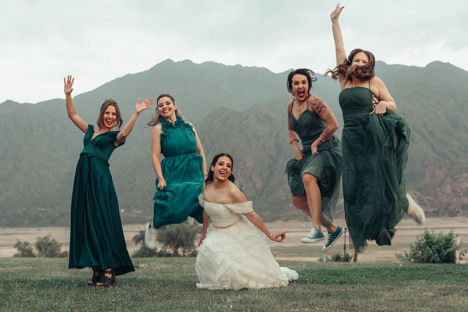 Wedding party jumps joyfully in coordinated teal dresses against a backdrop of majestic mountains. fotografos de boda en mendoza