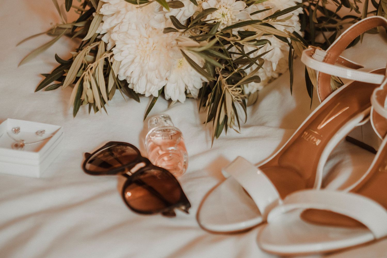 Wedding details including white flowers, sunglasses, and accessories arranged on a light wooden surface.