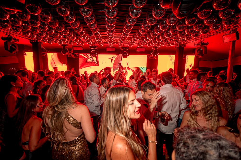 A crowded dance floor illuminated by red lighting with a honeycomb pattern ceiling at a wedding reception. fotografos de boda en mendoza