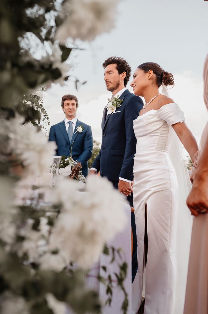 Wedding party stands in a line during outdoor ceremony with white floral decorations framing the scene. wedding in mendoza