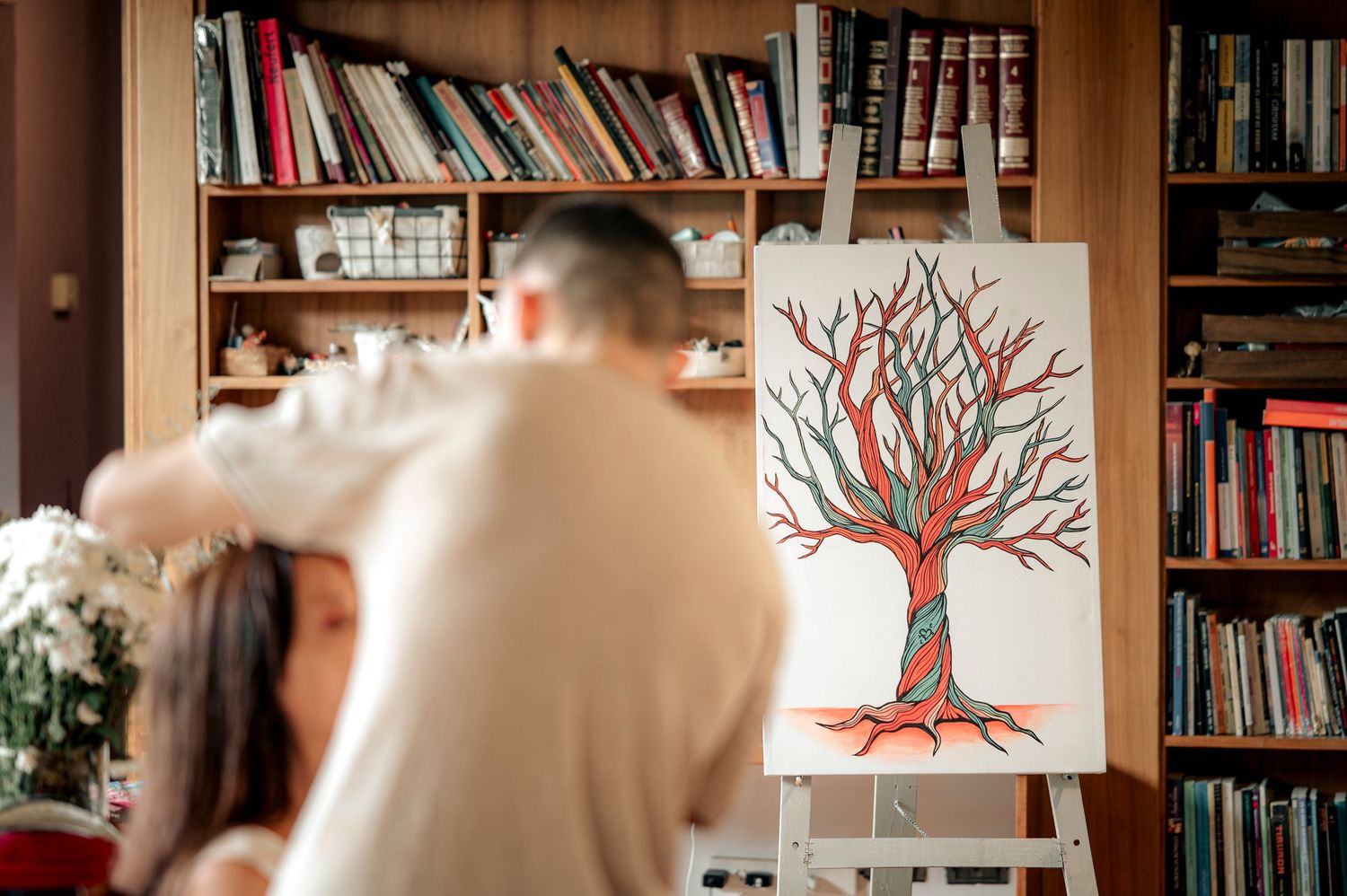 A cozy library interior with bookshelves lining the walls and a decorative red tree artwork displayed on white panels.