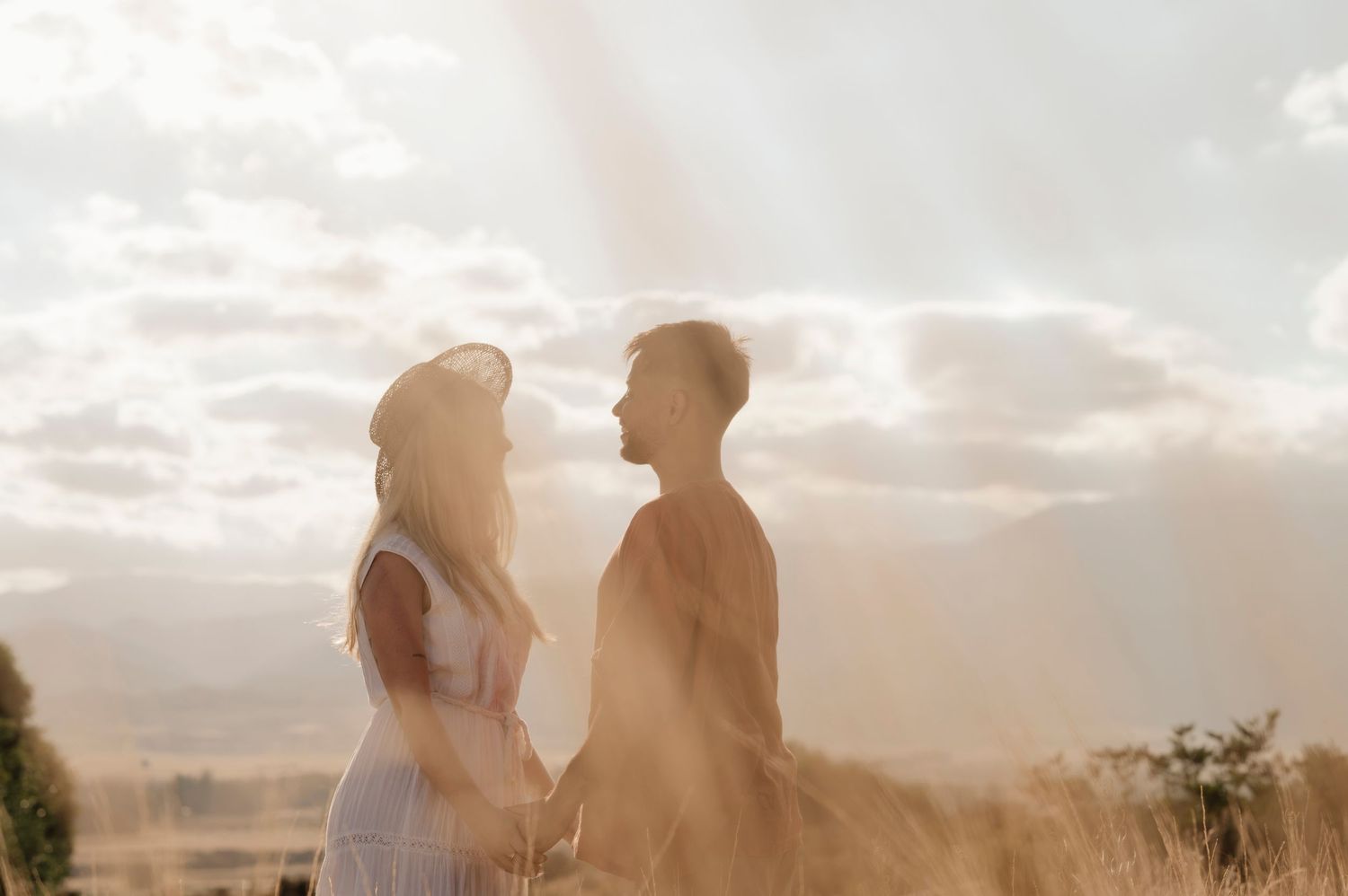 A romantic silhouette of a couple standing together against a cloudy sunset sky in a natural outdoor setting.