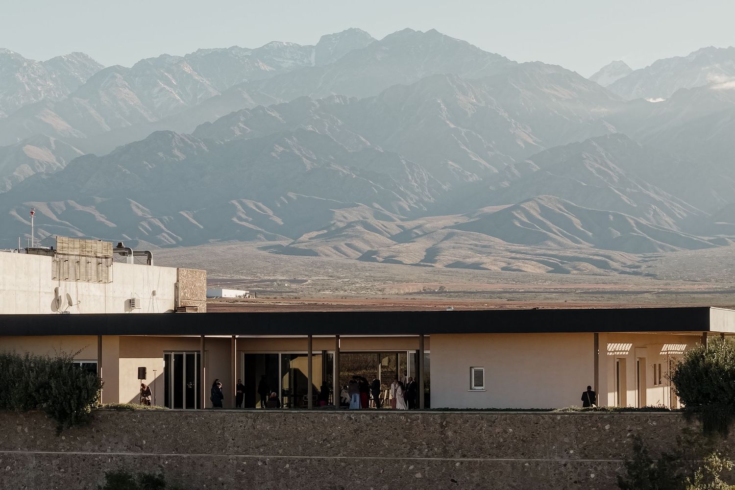 Modern building with people gathered on terrace, set against dramatic mountain landscape in arid desert region.fotógrafos de boda en Mendoza