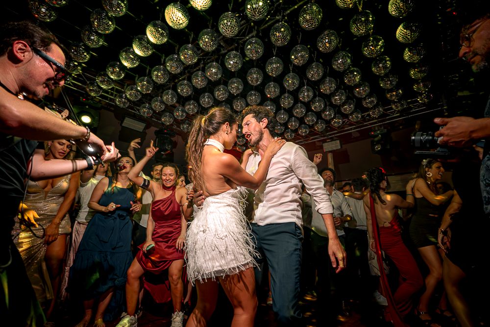 A lively dance party scene with people dancing in a dimly lit venue with string lights overhead. wedding in mendoza