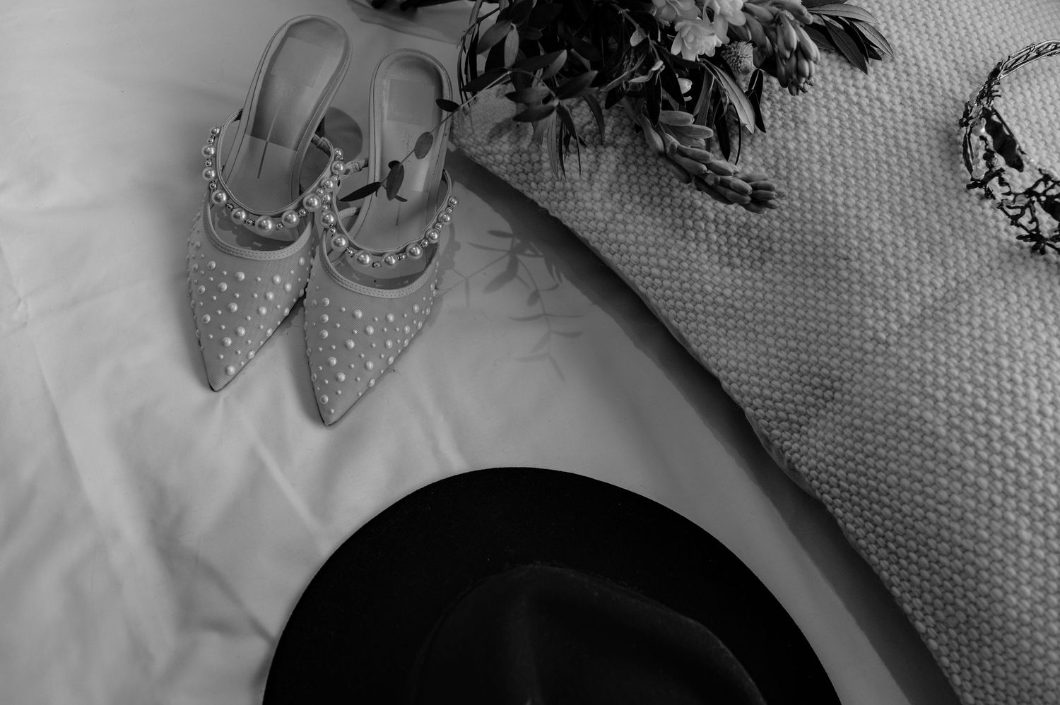 A pair of elegant silver glitter high heel shoes with pointed toes rests on a white textured surface.