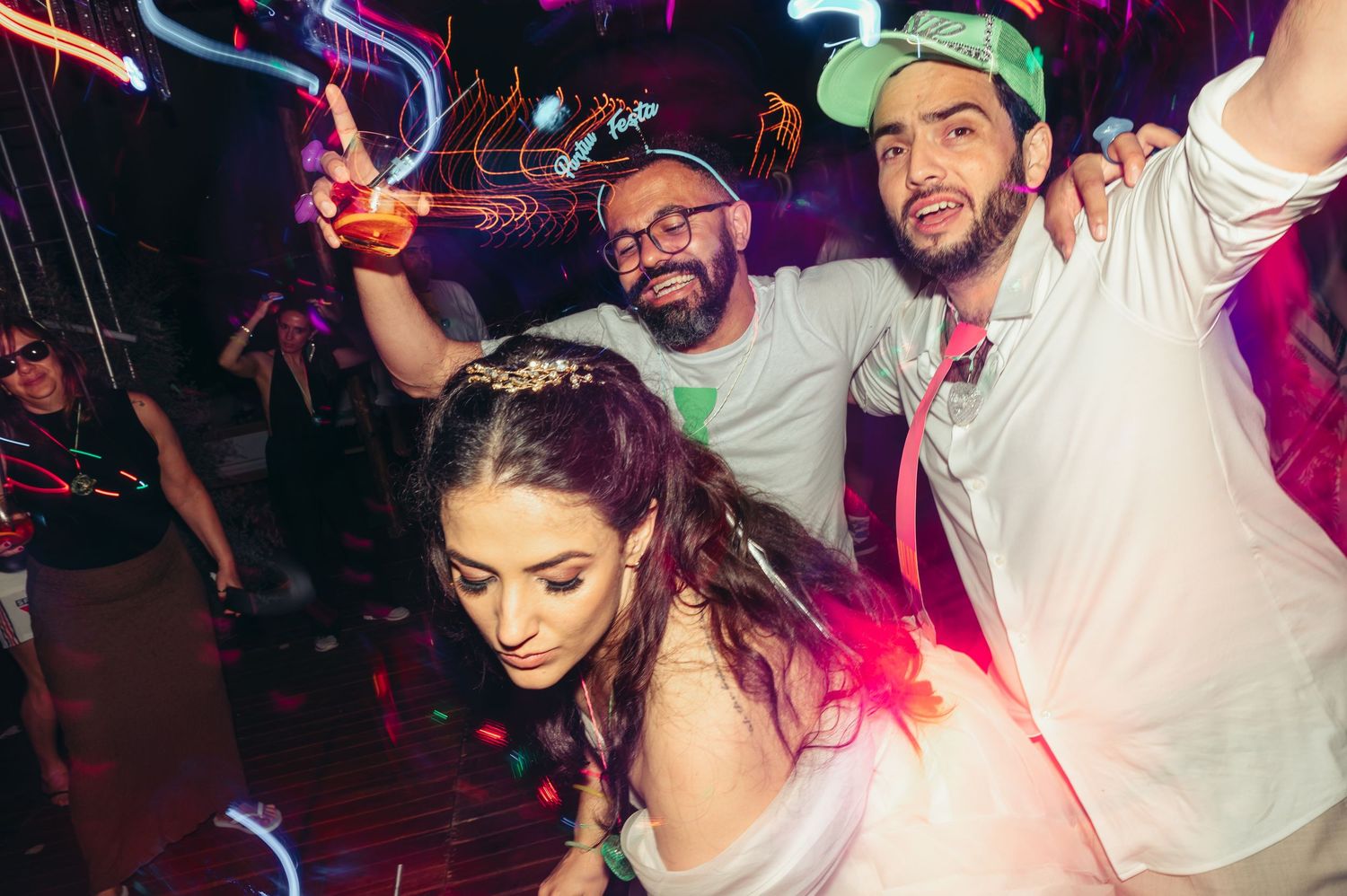 People dancing and celebrating at a nightclub with colorful purple and pink lighting effects.