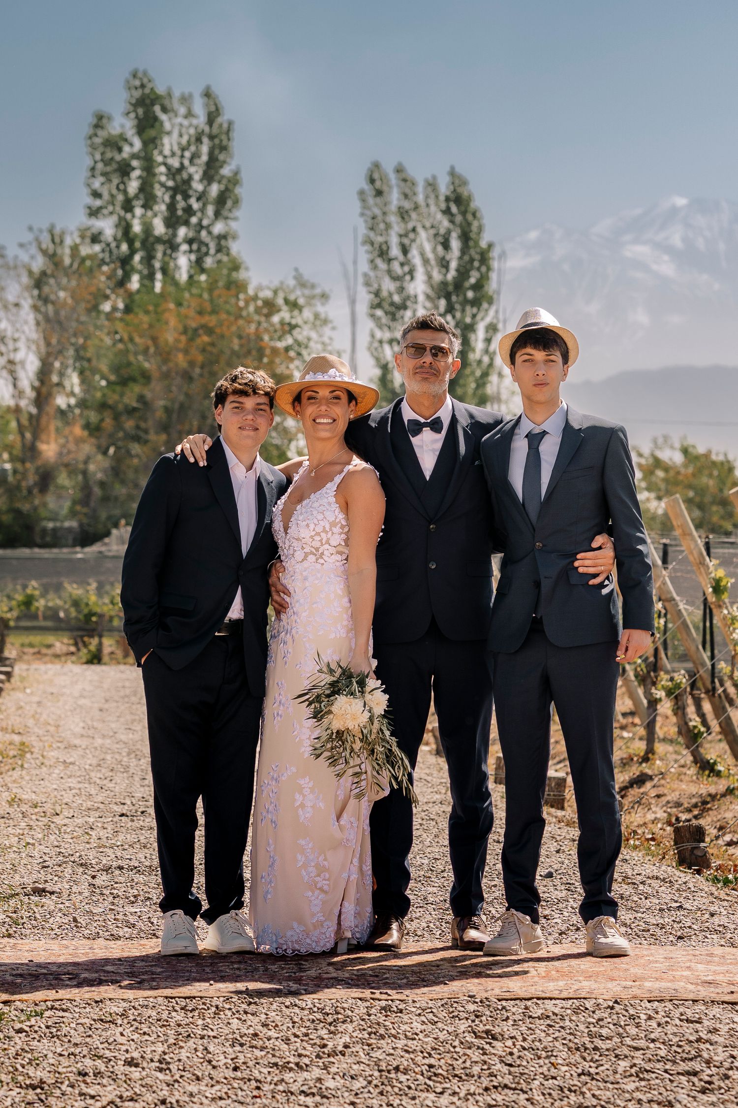 A group stands together on a dirt path with tall trees and mountains in the background on a sunny day.