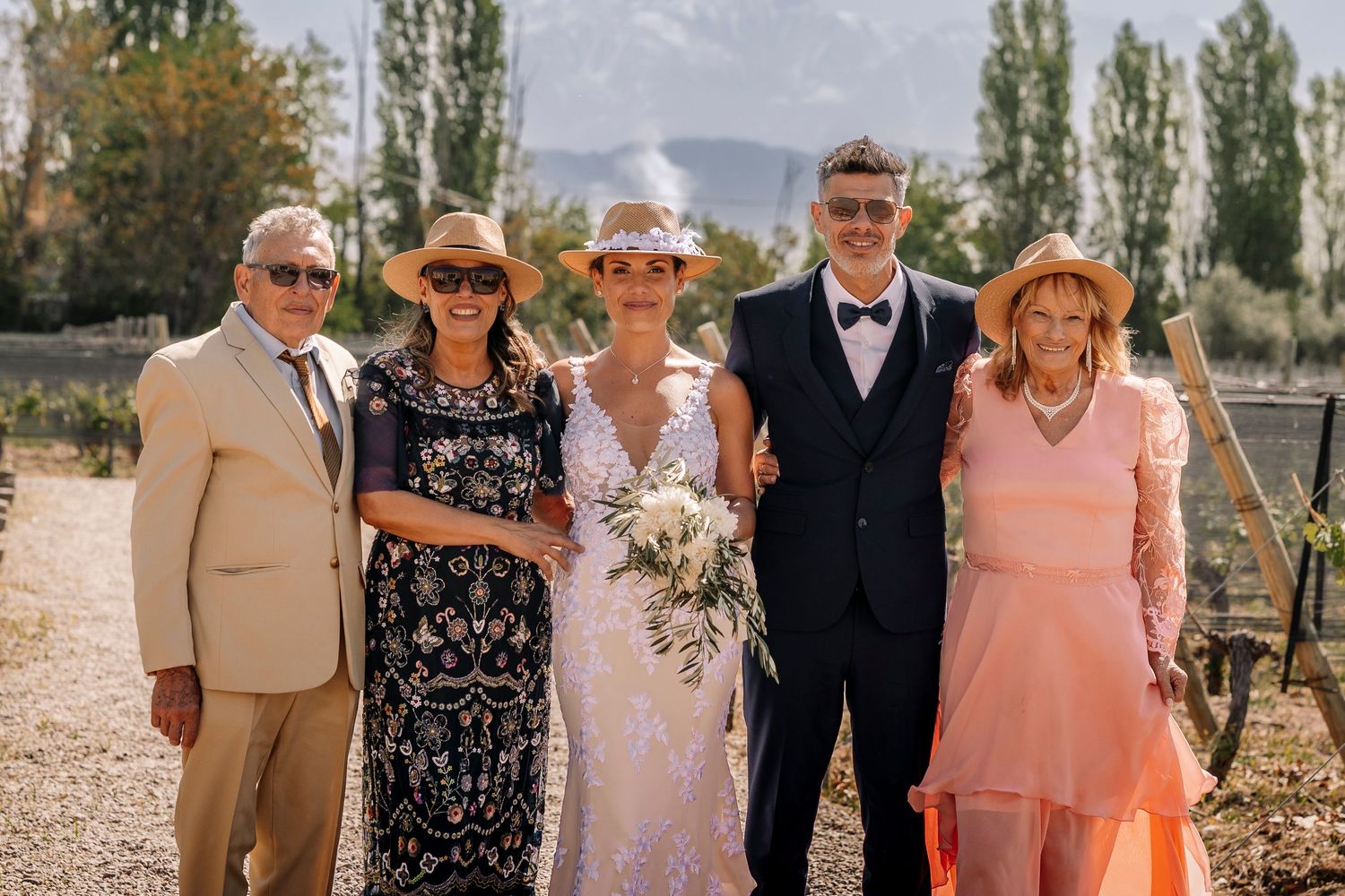 Group of wedding guests pose together outdoors in summer attire against a natural backdrop.