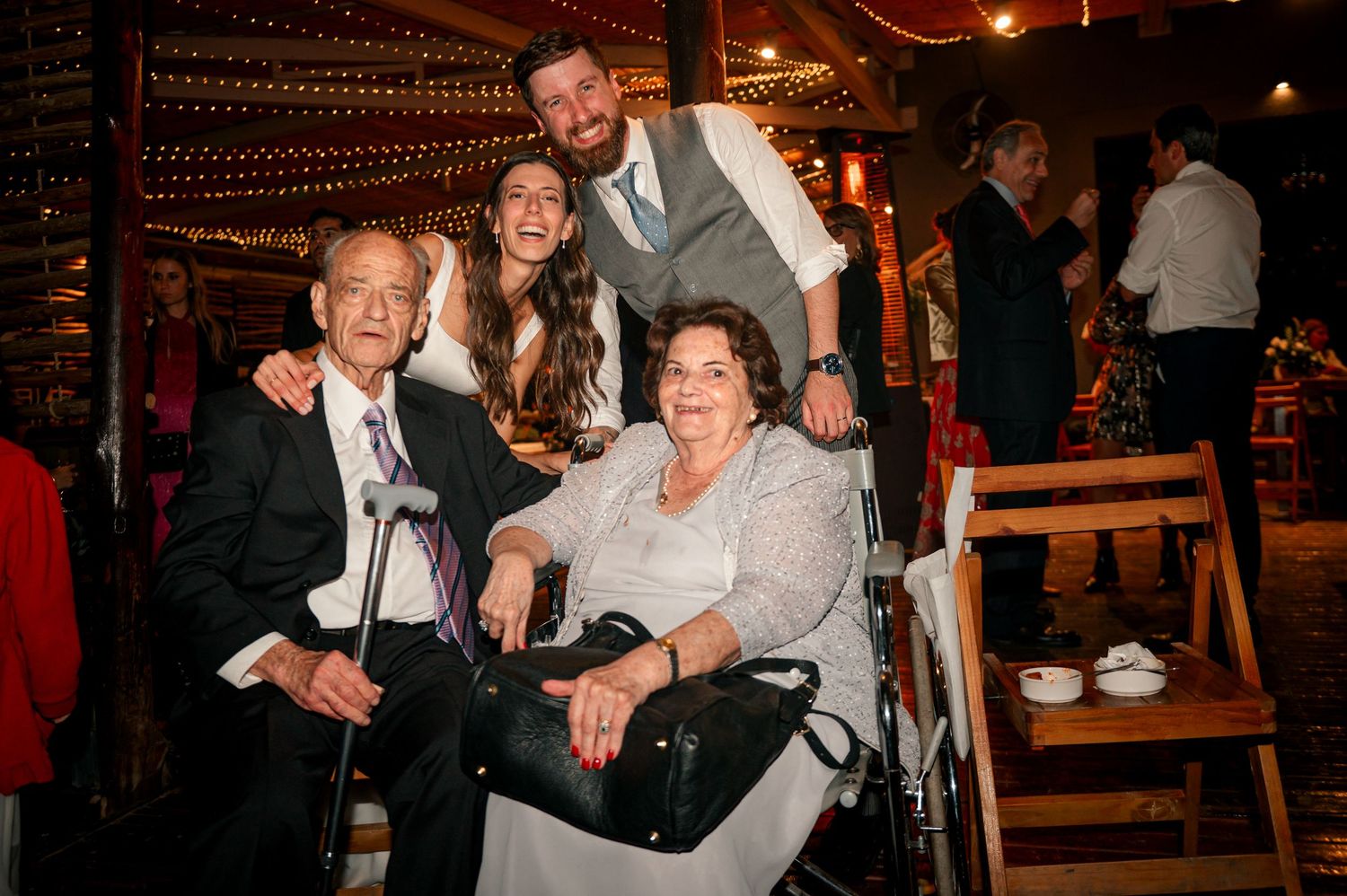 A group celebrating together at a dimly lit venue with string lights and wooden chairs in the background.